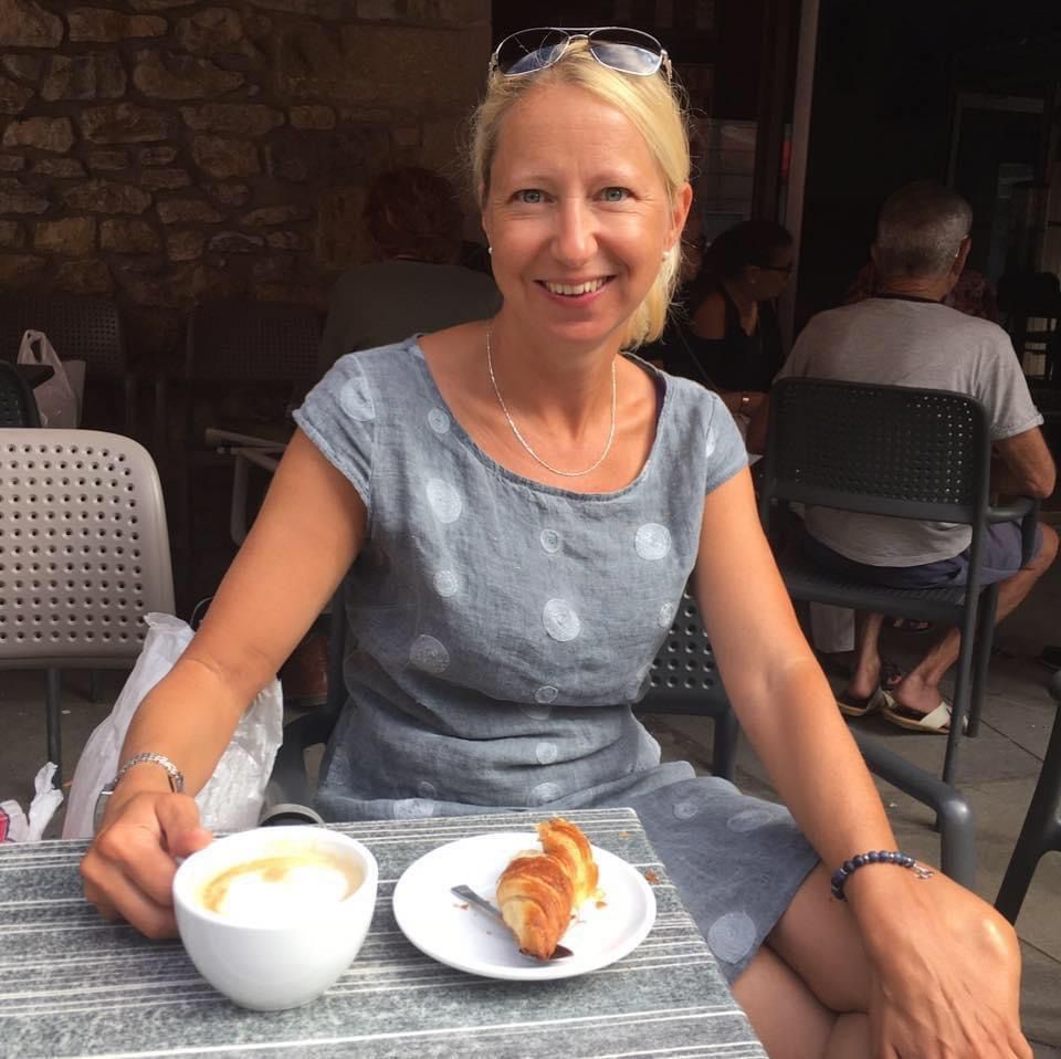 Daniela Meingaßner lächelnd in einem Straßencafé, vor ihr Cappuccino und Croissant
